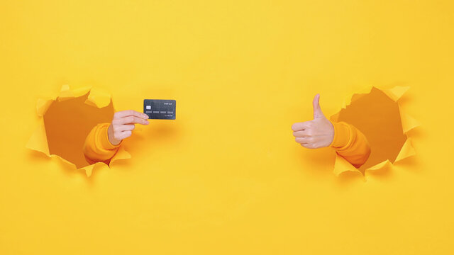 Woman hand arm hold credit bank card isolated through torn yellow wall orange background studio. Copy space advertisement place for text or image promotional content Advertising area workspace mockup