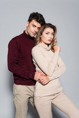  young couple in turtleneck jumpers embracing isolated on grey
