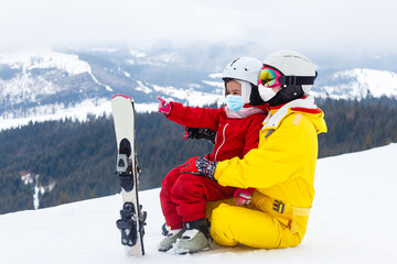 family wearing a medical mask during COVID-19 coronavirus on a snowy mountain at a ski resort