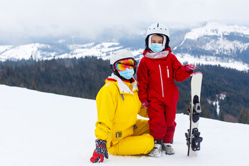 family wearing a medical mask during COVID-19 coronavirus on a snowy mountain at a ski resort