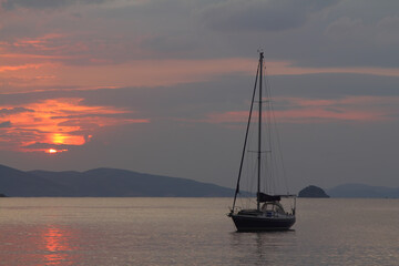 Alone sailboat at sunset. Atmospheric seascape with orange sun.