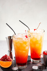 Ice tequila Sunrise cocktails on a gray concrete table, next to a jigger and cocktail cherry. Close-up, vertical orientation, selective focus, copy space.