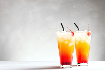 Two beautiful cocktails of tequila sunrise on a gray concrete background, horizontal orientation,...