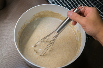 dough in white plastic plate and hand with whisk on dark wooden table