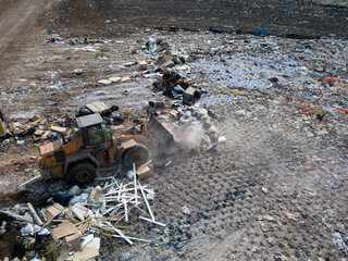 Top drone view of landfill. Different types of garbage on dump of big city. Tractor carries waste.