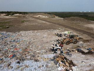 Aerial view of yellow buldozer on dumping site with different types of waste. Landfill of big city. Waste sorting.