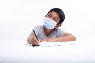 Schoolboy with a protective face mask writing in notebook at home, Homeschooling New Normal education concept 
