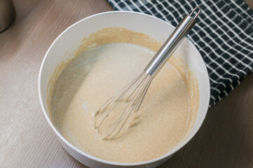 dough in white plastic plate and hand with whisk on dark wooden table