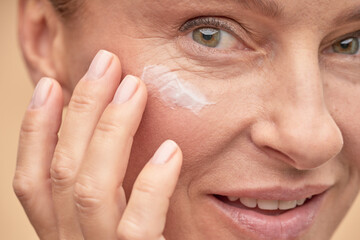 Happy beautiful lady applying anti-aging cream under the eyes