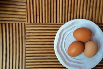White plate with three eggs on a wooden striped table