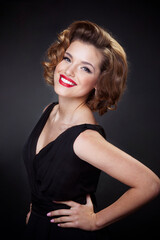Fototapeta premium Closeup portrait of a elegant, smiling young woman, model with charming hairstyle and evening make up, looking at camera, over black background.