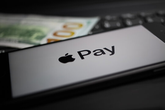 Viersen, Germany - April 9. 2020: Close up of mobile phone screen with logo lettering of Apple Pay payment provider on computer keyboard, blurred us dollar money background