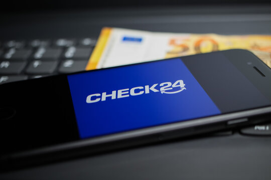 Viersen, Germany - April 9. 2020: Close up of mobile phone screen with logo lettering of Check24 comparison portal on computer keyboard, 50 Euro money background