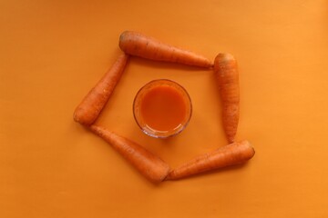 Carrot and carrot juice in a glass on a light orange background