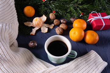 fir branches on the table near tangerines, a warm white sweater, a mug of coffee and nuts