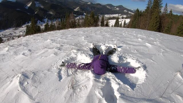 Happy woman make Snow Angel in winter mountain