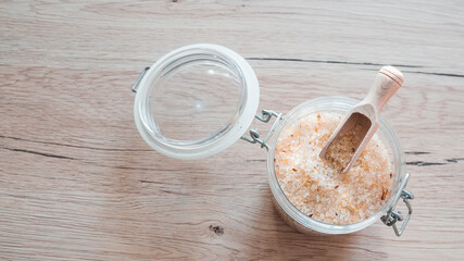 Sea salt in glass with wooden scoop on wooden table