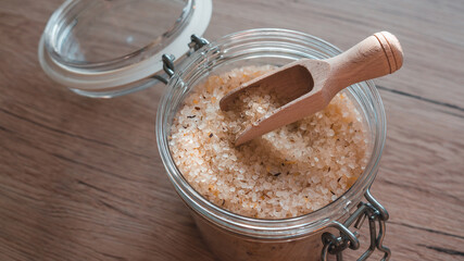 Sea salt in glass with wooden scoop on wooden table