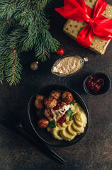 Swedish meatballs with mashed potatoes, gravy and lingonberry jam on dark background with Christmas decorations. Top view