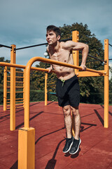 Young shirtless bodybuilder doing dips on parallel bars during his workout in a modern calisthenics...