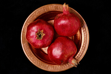 Flat lay with fresh pomegranates on a copper metal plate against a black background. Harvesting fruits, top view