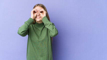 Young blonde woman isolated on purple background showing okay sign over eyes