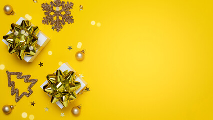 Happy xmas. White gift box with golden color ribbon, New Year balls and sparkling lights in Christmas composition on dark yellow background for greeting card. Copy space. Winter holidays, New Year.