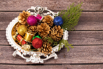Christmas Decoration Ornaments Like Golden Conifer Pine Cones Green Leaves Drums Glitter Balls In Silver Color Designer Tray On Rustic Dark Brown Wooden Background And Copy Space For Custom Text