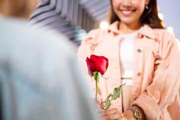 Smiling attractive Asian woman looks happy and surprise receiving rose flower from her boyfriend for Valentine's day or proposal. love and togetherness concept. focus on rose