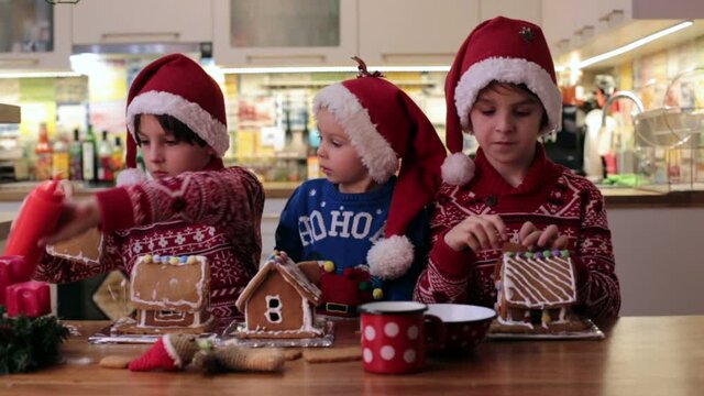Children, boys, decorating home made ginger bread houses at home with mom helping them