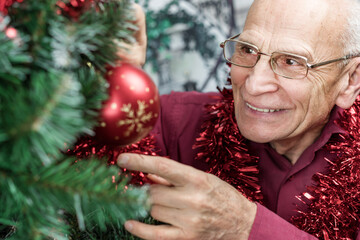 elder man wearing eyeglasses with smile on face hanging red ball on Christmas tree