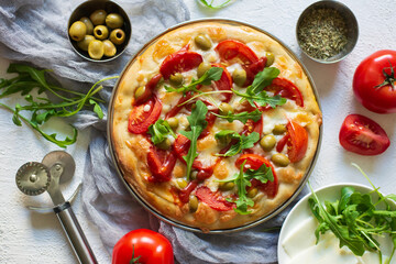 Top view of delicious pizza Margarita a dish of yeast dough stuffed with tomatoes, mozzarella, olives, ketchup, arugula on a light textured background
