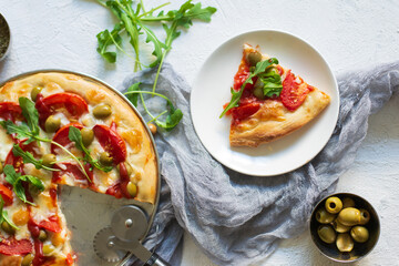 Top view of delicious pizza Margarita a dish of yeast dough stuffed with tomatoes, mozzarella, olives, ketchup, arugula on a light textured background