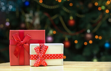 Coffrets cadeaux rouges et blancs avec des arcs sur une table en bois. Lumières orange de bokeh de fond sur un arbre de Noël