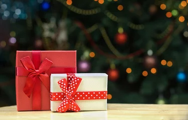 Photo sur Plexiglas Doux monstres Coffrets cadeaux rouges et blancs avec des arcs sur une table en bois. Lumières orange de bokeh de fond sur un arbre de Noël