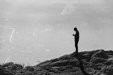 Young man standing on top of the mountain and looking at his android phone