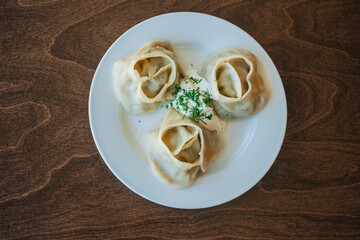 Large manti on a white dish with sour cream and herbs. Eastern cuisine. Meat in dough. Stands on a wooden table