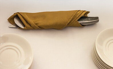 Cake knife and spatula wrapped in a linen napkin and white plates against a white tablecloth closeup