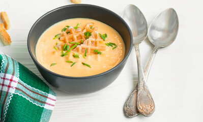 Cheese soup with crackers and herbs. Cream soup on a light wooden table. Copy space.