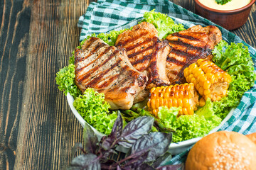 Grilled steaks with herbs and vegetables on a dark wooden background. Copy space.
