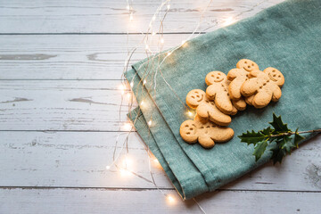 a stack of gingerbread cookies or ginger-man on a white table and green cloth with Christmas lights, with copy space - 396639233