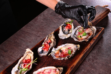 The cook adds micro-greens to the oysters. Two types of oysters with savory sauces on a wooden Board. Stylish serving of dishes. Oyster season. Unrecognizable photo.