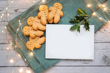 a stack of gingerbread cookies or ginger-man with blank white card for copy space on a white table and green cloth with Christmas lights - 396639298