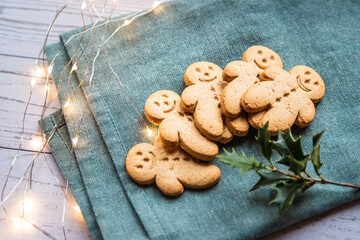 a stack of gingerbread cookies or ginger-man on a white table and green cloth with christmas lights - 396639466