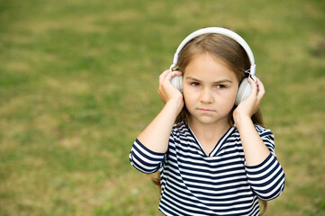 Serious cute child listen to music playing in headphones summer landscape outdoors, sound, copy space