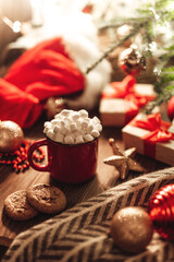 Christmas red mug with cocoa and marshmallows and cookies on a wooden table. New Year's still life with a Christmas tree, a Santa hat and festive decorations.