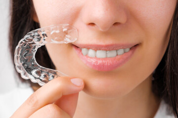 Close up woman holding a transparent removable braces for perfect smile. Orthodontic aligners for...