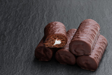 Chocolate sponge cake covered with milk chocolate on black stone background