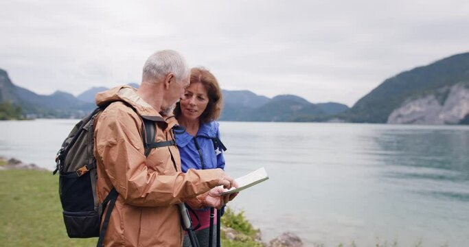 Senior pensioner couple by lake with hiking in nature, using map.