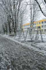 Snowy pedestrian alley with empty swings near the school. Lutsk, Ukraine. Vertical image.